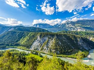 Luftaufnahme der Rheinschlucht mit weißen Kalksteinfelsen, grünen Wäldern und türkisfarbenem Fluss zwischen Bergen unter blauem Himmel.