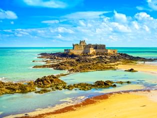 Festung Fort National auf felsiger Insel bei Ebbe in Saint-Malo, umgeben von türkisfarbenem Wasser, Sandstrand und freiliegenden Felsen.