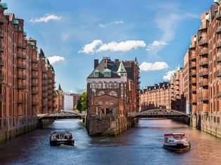 Kanal in der Hamburger Speicherstadt mit roten Backsteinspeichern auf beiden Seiten, zwei Brücken und Ausflugsbooten auf dem Wasser.
