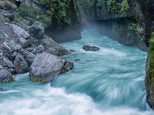 Türkisfarbene Aare rauscht durch die enge Aareschlucht mit steilen, moosbewachsenen Felswänden und großen Felsbrocken im Wasser.