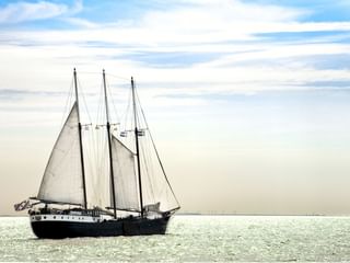 Traditionelles Segelschiff Mare fan Fryslan mit dunklem Rumpf und drei weißen Segeln auf ruhigem Wasser unter bewölktem Himmel.