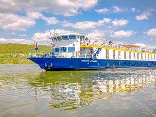 Flusskreuzfahrtschiff MS Prinzessin Katharina mit blauem Rumpf und weißem Aufbau fährt auf der Donau unter teilweise bewölktem Himmel.