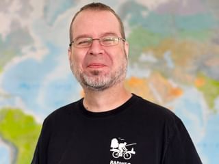Portrait von Michael K. mit Brille und schwarzem Radfahrer-Shirt mit Weltkarte im Hintergrund.