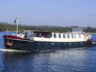 MS Lena Maria, ein Passagierschiff mit dunkelblauem Rumpf und weißem Aufbau, fährt auf einem Fluss mit Bäumen am Ufer.