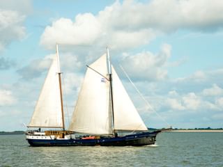 Traditionelles niederländisches Segelschiff Wapen fan Fryslân mit dunkelblauem Rumpf und weißen Segeln auf ruhigem Wasser unter bewölktem Himmel.