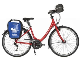 Rotes Tourenrad mit tiefem Einstieg, 27-Gang-Schaltung, Frontkorb, blauer Packtasche mit Radweg Reisen Logo und Ständer vor weißem Hintergrund.