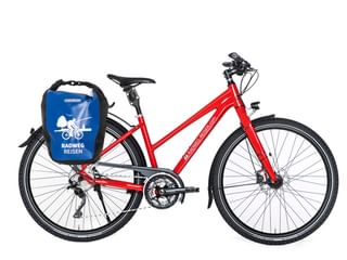 Rotes Fahrrad mit Trapezrahmen, 30-Gang-Schaltung, Scheibenbremsen, Schutzblechen und blauer Radweg-Reisen-Tasche am Gepäckträger vor weißem Hintergrund.