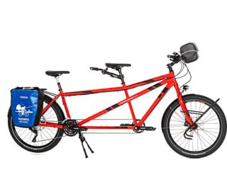 Rotes Tandem-Fahrrad mit zwei Sitzen, schwarzen Sätteln, blauen Gepäcktaschen, grauer Lenkertasche und Ständer vor weißem Hintergrund.