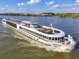 Weißes Flusskreuzfahrtschiff MS Lisabelle fährt auf einem breiten Fluss unter blauem Himmel mit Wolken. Das moderne Schiff hat mehrere Decks und Panoramafenster.