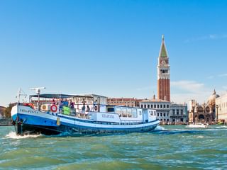 Blaues Kreuzfahrtschiff MS Vita Pugna in der Lagune von Venedig mit Markusturm und historischen Gebäuden im Hintergrund.