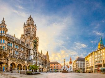 Münchens Marienplatz mit dem verzierten Turm des Neuen Rathauses links und umliegenden historischen Gebäuden unter blauem Himmel.