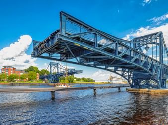 Blaue Stahlkonstruktion der Kaiser-Wilhelm-Brücke in hochgeklappter Position über Wasserstraße in Wilhelmshaven unter sonnigem Himmel.