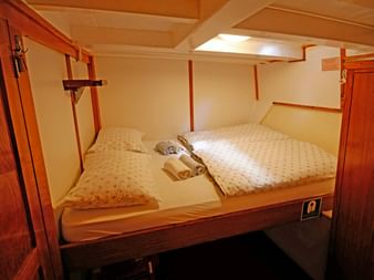 Kompakte Doppelkabine auf der MS Orkan mit zwei Etagenbetten, weißer Bettwäsche, Holzverkleidung und einem Schrank. Handtücher liegen auf jedem Bett.