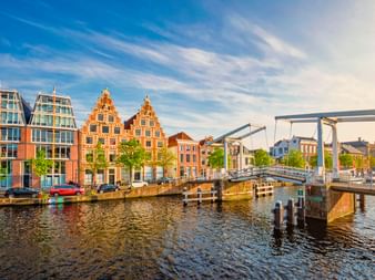 Weiße Zugbrücke Gravestenenbrug über Kanal in Haarlem mit historischen niederländischen Giebelhäusern und modernen Gebäuden am Ufer unter blauem Himmel.
