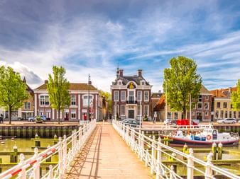 Weiße hölzerne Zugbrücke Raadhuisbrug führt zu historischen Hafengebäuden in Harlingen, Niederlande, mit Booten am Kanal.
