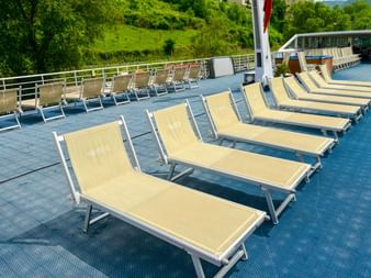 Sonnendeck der MS Normandie mit Reihen cremefarbener Liegen auf blauem Boden. Grüne Hügel im Hintergrund entlang des Flusses.