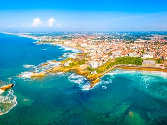 Aerial view of French Atlantic coastal town with rocky shoreline, sandy beaches, and turquoise ocean waters under blue sky.