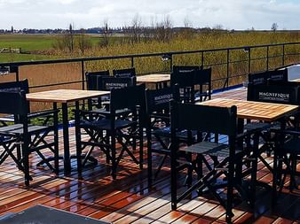 Sonnendeck der MS Magnifique IV mit schwarzen Klappstühlen und Holztischen auf bunt gestreiftem Deck mit Blick auf grüne Landschaft.