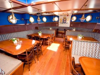 Speisesaal an Bord der Mare fan Fryslân mit Holztischen, gemusterten Bänken, Bullaugenlampen an blauen Wänden und friesischem Wappen.