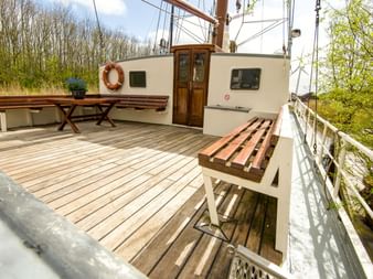 Holzdeck des Dreimastklippers Elizabeth mit Holzbänken, Kabineneingang und Takelage. Bäume im Hintergrund sichtbar.