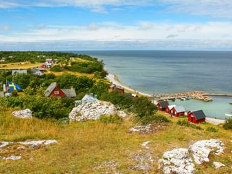 Malerischer Blick auf das Dorf Hallshuk auf Gotland mit roten Holzhäusern, schwedischer Flagge, weißen Kalksteinfelsen und Ostseeküste.