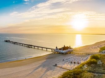 Luftaufnahme der Seebrücke Ahlbeck in der Ostsee bei Sonnenuntergang, mit Sandstrand, Strandkörben und Küstenlinie der Insel Usedom.