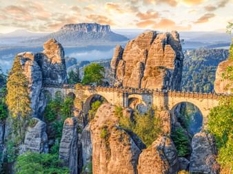 Basteibrücke zwischen Felsformationen im Elbsandsteingebirge. Steinbögen verbinden hohe Sandsteinsäulen umgeben von Wald und Bergen.