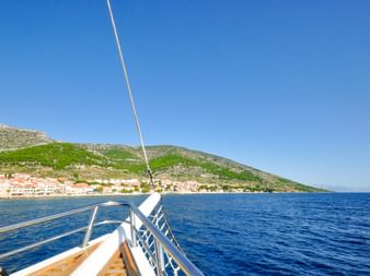 Blick vom Bootsdeck auf kroatische Küstenstadt mit rotgedeckten Häusern am Hang, tiefblauem Adriatischem Meer und klarem Himmel bei Split.