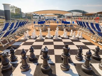 Sonnendeck der MS Lisabelle mit übergroßem Schachspiel auf Schachbrett, blauen Liegestühlen und Brücken im Hintergrund.