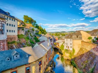 Luftaufnahme der Saarburger Altstadt mit traditionellen Gebäuden entlang eines schmalen Kanals. Historische Häuser mit bunten Fassaden säumen den Wasserweg.