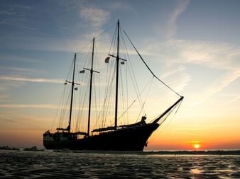 Silhouette des dreimastigen Segelschiffs Mare fan Fryslan auf ruhigem Wasser bei Sonnenuntergang mit orangefarbenem und blauem Himmel.