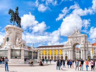 Praça do Comércio in Lissabon mit Reiterstatue, Arco da Rua Augusta und gelben Gebäuden. Touristen versammeln sich unter blauem Himmel.