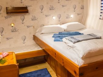 Gemütliche Kabine auf der MS Panagiota mit Doppelbett, weißen Kissen, maritimer Tapete, Holzmöbeln, Spiegel und Fenster mit weißen Vorhängen.