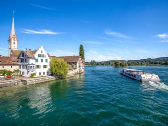 Passagierschiff auf dem Rhein in Stein am Rhein mit historischen Ufergebäuden und weißem Kirchturm unter blauem Himmel.