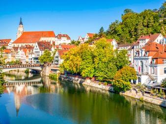 Blick auf Tübingens Altstadt mit bunten Fachwerkhäusern entlang des Neckars. Eine Kirche mit rotem Dach überragt die Gebäude.