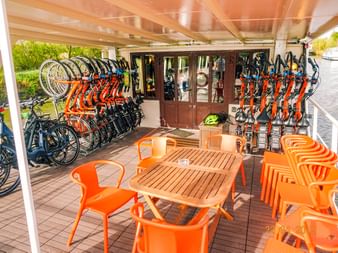 Außendeck der MS L'Estello mit orangen Klapprädern an beiden Wänden, Holztischen, orangen Plastikstühlen und Glastüren zum Innenbereich.