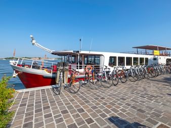 Weißes Flusskreuzfahrtschiff MS Ave Maria am Anleger mit Fahrradreihen auf dem Steinpier unter blauem Himmel.