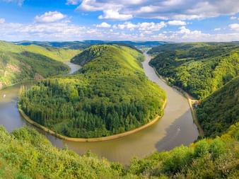 Panoramablick auf die Saarschleife bei Mettlach mit einer markanten Flussschleife der Saar, umgeben von bewaldeten Hügeln.