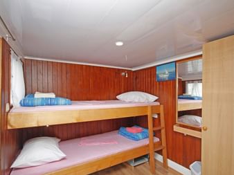 Kompakte Schiffskabine auf MS Kazimir mit Holzwänden, Etagenbetten mit weißen Kissen und blauen Decken sowie hellem Holzschrank.