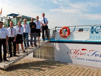 Sieben Crew-Mitglieder in weißen Uniformen stehen auf der Gangway des Flusskreuzfahrtschiffs MS Fluvius mit sichtbarem Rettungsring.