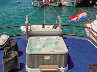 Whirlpool auf dem Sonnendeck der MS Azimut mit blauem Teppich, Korbstühlen und kroatischer Flagge. Türkisfarbenes Wasser und Boote im Hintergrund.