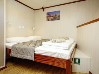 Saubere Kabine auf der MS Aria mit Doppelbett, beigen Wänden, Holzboden und gefalteten Handtüchern. Ein Bild mit Segelbooten hängt über dem Bett.