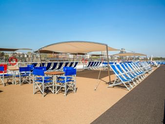 Sonnendeck der MS Lisabelle mit blau-weiß gestreiften Liegen, Klappstühlen und beigen Sonnensegeln. Klarer blauer Himmel über dem Deck.
