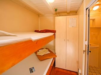 Kompakte Kabine auf der MS Dalmatino mit Etagenbetten in Orange und Weiß, weißem Kleiderschrank und Bad durch offene Tür sichtbar.