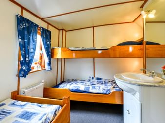 Kabine auf Klipper Elizabeth mit Etagenbett, Einzelbett, Waschbecken und maritimen blauen Vorhängen. Holzvertäfelte Wände und Bettwäsche mit blauen Mustern.
