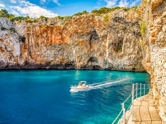 Türkisfarbene Wasserbucht bei der Grotta Zinzulusa nahe Castro mit Kalksteinklippen, einem Boot im Wasser und Steinstufen mit Geländer.