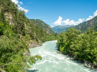 Turquoise Inn River flowing through a valley in Austria, surrounded by green forests and mountains under a blue sky with white clouds.