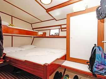 Kompakte Dreibettkabine auf der MS Aneta mit hölzernen Etagenbetten, weißer Bettwäsche, holzverkleideten Wänden, einem Schrank und Stauraum unter dem unteren Bett.
