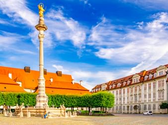 Mariensäule mit goldener Statue auf dem Platz in Eichstätt, umgeben von historischen Gebäuden mit orangen Dächern und grünen Bäumen.