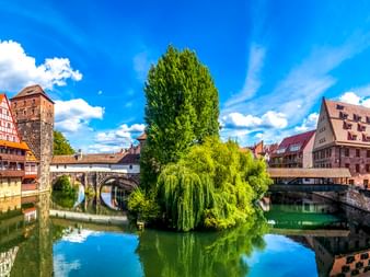 Malerischer Blick auf den Henkersteg und mittelalterliche Gebäude entlang der Pegnitz in Nürnberg mit Fachwerkhäusern und grünen Bäumen.